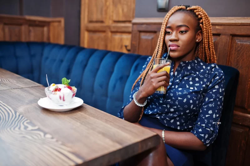 Portrait of beautiful young african business woman with dreadlocks wearing blue blouse and skirt sitting in cafe with ice cream and pineapple juice Free Photo