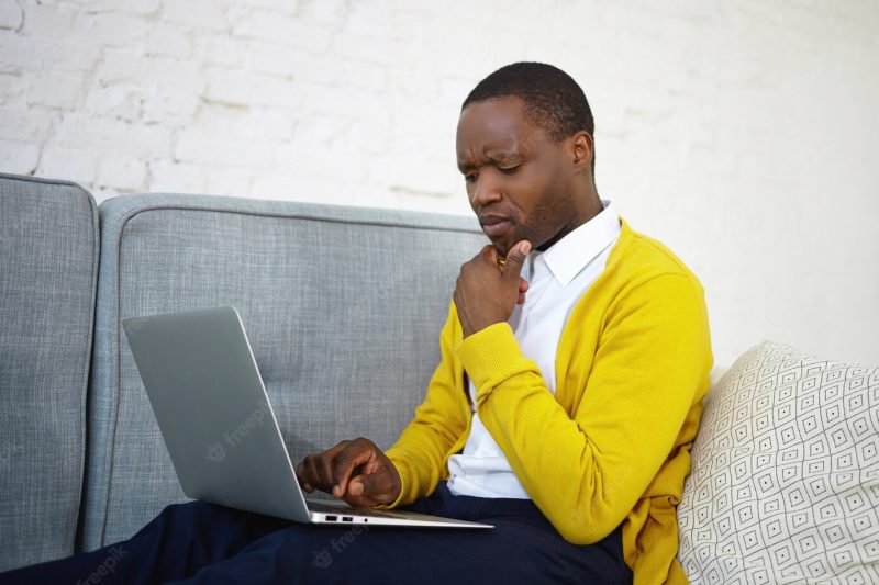 Portrait of frustrated frowning afro american freelancer having some computer problem while working remotely using laptop on sofa. people, lifestyle, freelance, modern technology and communication Free Photo