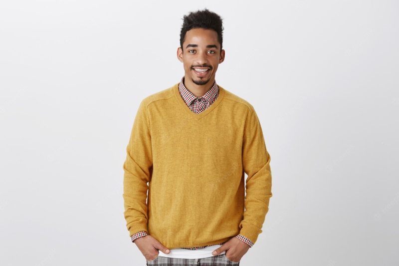 Portrait of good-looking African-American with Afro hairstyle in stylish yellow pullover holding hands in pockets, smiling casually Free Photo