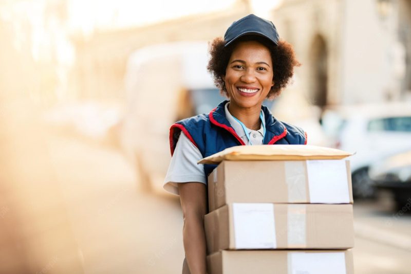 Portrait of happy black courier delivering packages and looking at the camera Free Photo