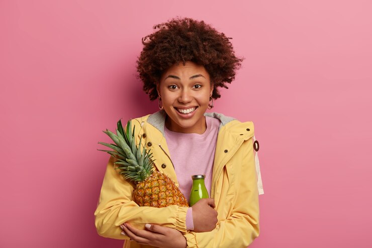 Portrait Joyful Curly Woman Embraces Fresh Juicy Pineapple Green Smoothie Made Fruit Wears Yellow Anorak Smiles Positively 273609 39062