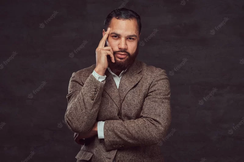 Portrait of a pensive african-american man, dressed in a classic brown jacket standing in a studio on a dark background. Free Photo