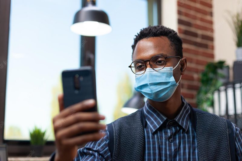 Portrait of startup office worker with glasses wearing face mask holding smartphone in online interview. focus on entrepreneur in isolation in video call looking at mobile phone screen. Free Photo