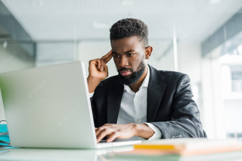 Portrait of young African man typing on laptop in office Free Photo