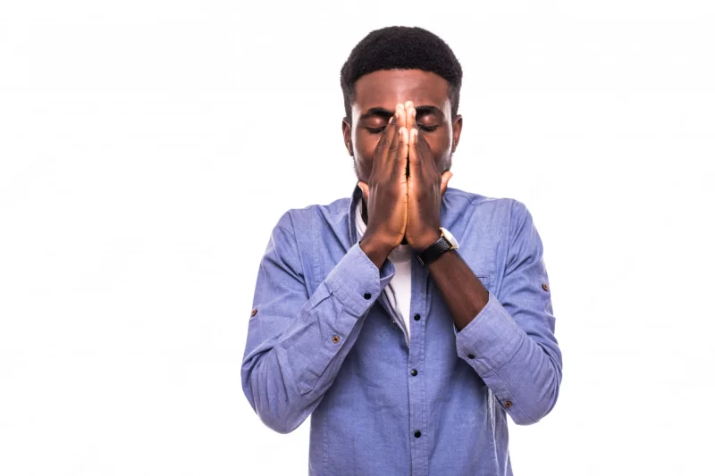 Portrait of young Afro-American man in checkered shirt covering his mouth with both hands and looking with shocked and guilty expression as if he did something wrong, standing at blank chalkboard Free Photo