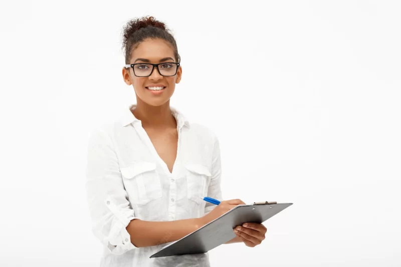 Portrait of young successful african business lady in glasses smiling, writing to folder, looking at camera on white Free Photo