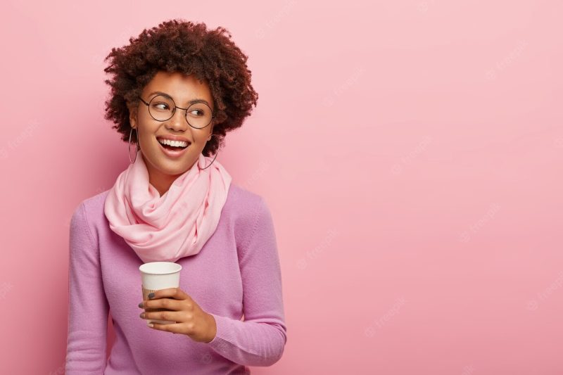 Positive relaxed curly female worker enjoys coffee break, has talk with colleague Free Photo