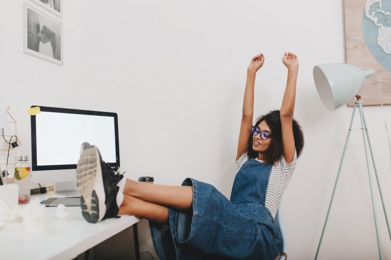 Pretty girl in vintage denim clothes relaxing with legs on table and hands up Free Photo