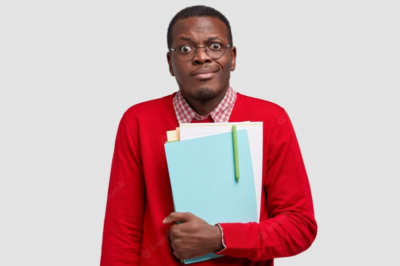 Puzzled dark skinned man carries notepad, looks with frustrated expression Free Photo