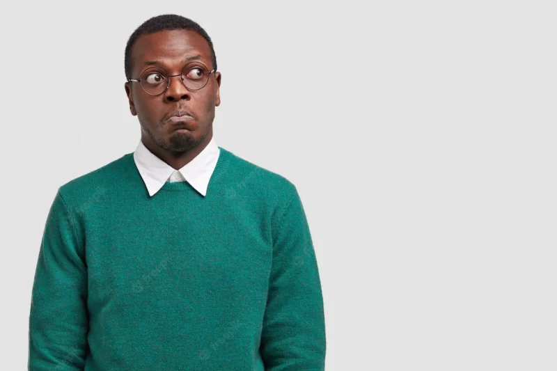 Puzzled dark skinned man looks thoughtfully and with bewilderment, focused aside, dressed in casual sweater Free Photo