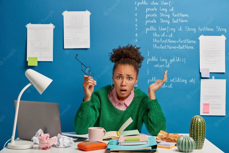 Puzzled indignant office worker feels confused with operational software problems, looks in panic, afraids of data loss, makes notes in notepad, raises both hands Free Photo