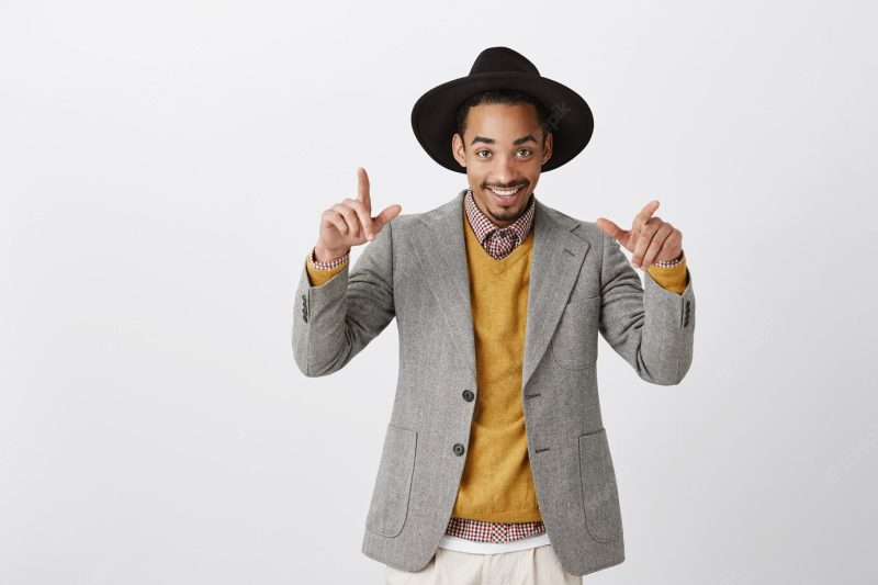 Ready to chill at sassy party. portrait of wealthy good-looking african-american in stylish outfit and round hat, making cool gestures while dancing or hanging out with friends over gray wall Free Photo