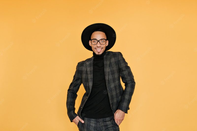 Relaxed african guy in vintage checkered suit smiling on yellow wall.excited black young man in hat having fun during photo shoot. Free Photo