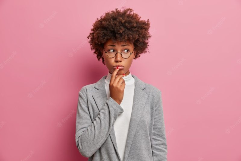 Sad discontent curly woman executive worker looks unhappily aside, purses lips, expresses regret, has problem, needs good advice, dressed formally Free Photo