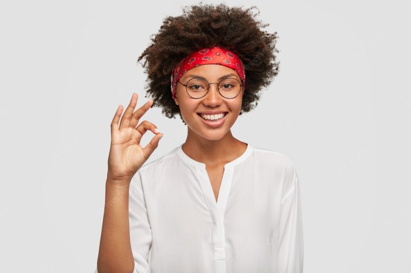 Satisfied ethnic female worker makes okay gesture, has work under control Free Photo