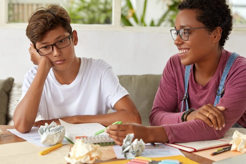 School and education concept. pleased experienced female teacher helps youngster to catch up with group, explains grammar rule, makes notes in notepad. teenager feels apathy as doesn’t want to study Free Photo