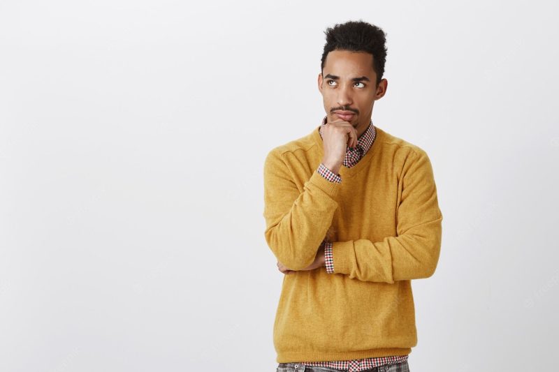 Seeking solution in mind. portrait of troubled attractive dark-skinned male with curly haircut leaning face on jaw, looking up and thinking, being bothered with thoughts over gray wall Free Photo