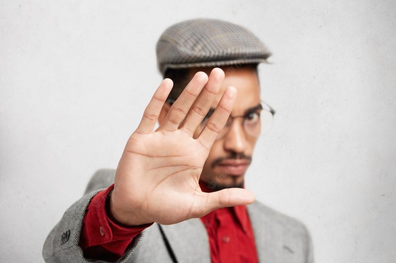 Selective focus on palm. strict mixed race male in round eye-wear, shows stop sign with hand Free Photo