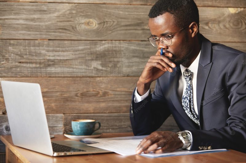 Serious African American businessman looking at laptop screen and thinking Free Photo