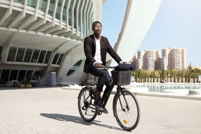 Serious and confident young African American male office worker wearing mirrored lens shades and formal black suit cycling Free Photo