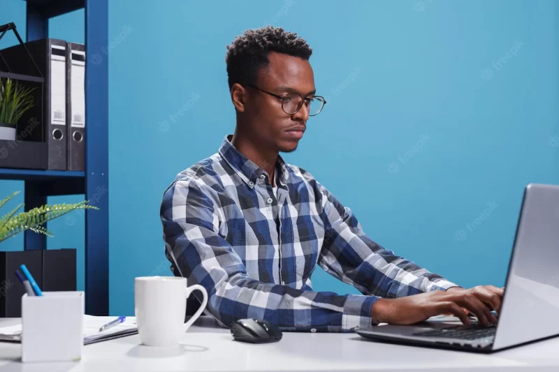 Serious firm project manager sitting at desk in modern office while using laptop to develop marketing strategy. confident company employee using work computer to analyze accounting documentation. Free Photo