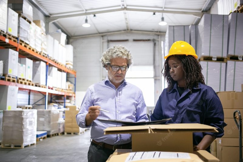 Serious mature inspector consulting black female employee during his checking of warehouse and completing form. copy space, front view. labor and inspection concept Free Photo