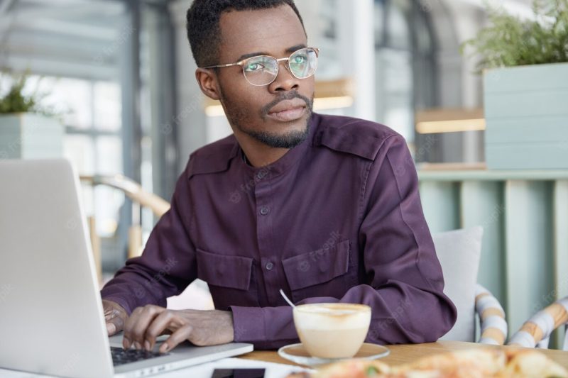 Serious thoughtful dark skinned businessman focused on work issues, keyboards information on laptop computer Free Photo