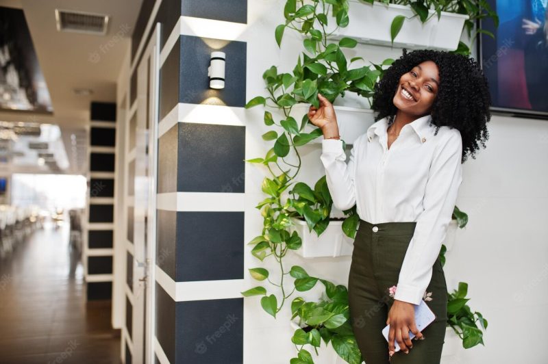 Sheerful business African American lady with afro hair wear white blouse and green pants posed in cafe with mobile phone at hand Free Photo Sheerful business African American lady with afro hair wear white blouse and green pants posed in cafe with mobile phone at hand Free Photo