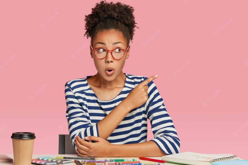 Shocked afro american woman thinks on blueprint creation, makes illustration with crayons Free Photo