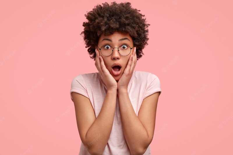 Shocked emotive woman keeps hands on cheeks Free Photo