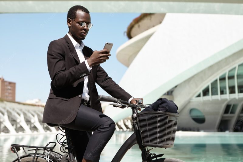 Side view portrait of modern ecologically conscious afro american banker commuting to work on bicycle, having carefree and joyful look. attractive black businessman in formal wear riding bike Free Photo