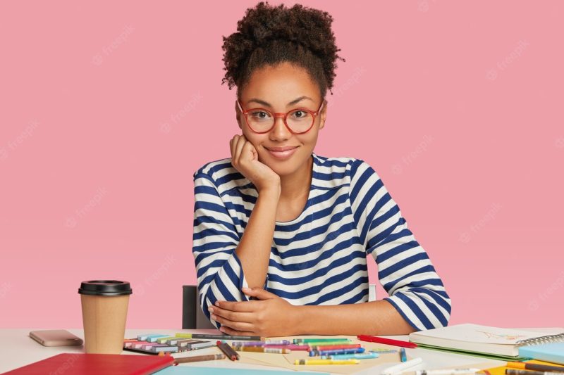 Shocked afro american woman thinks on blueprint creation, makes illustration with crayons Free Photo