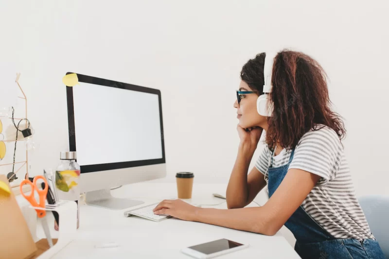 Slim black girl in headphones looking at computer’s screen with attention Free Photo