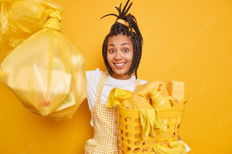 Smiling afro american woman with dreadlocks enjoys housework holds polythene bag Free Photo