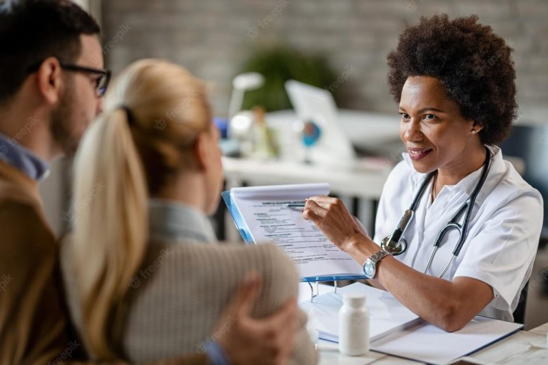 Smiling black female doctor talking to a couple while analyzing their medical reports during consultations at clinic Free Photo