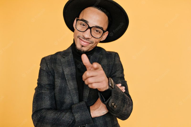 Smiling confident african man pointing finger . portrait of handsome male model with brown skin isolated on yellow wall. Free Photo