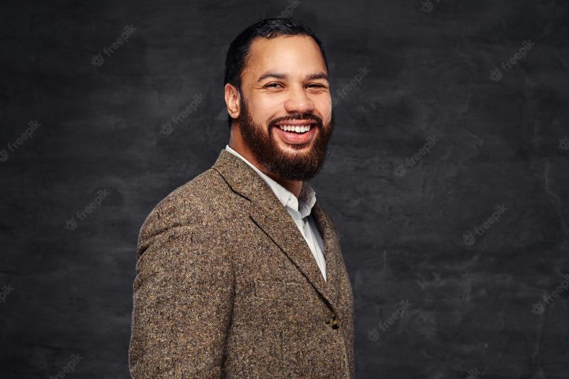 Smiling handsome bearded african-american businessman in a brown classic jacket. isolated on a dark background. Free Photo