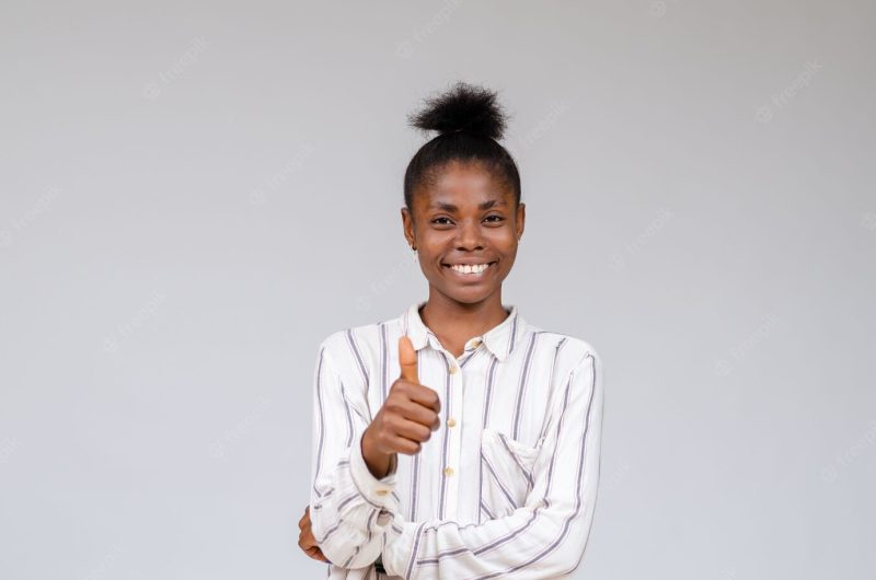 Smiling nigerian woman celebrating success with thumbs up Free Photo