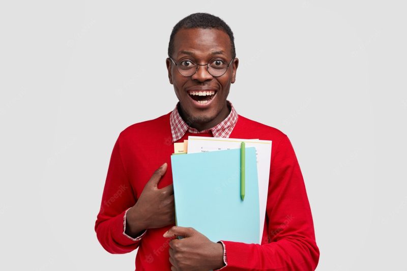 Smiling pleased male scientific worker keeps hand on chest, carries papers and notebook with pen, cant believe in his success, has joyful facial expression, wears round glasses Free Photo