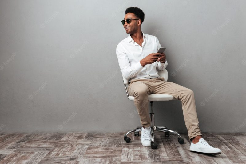 Smiling young African man sitting in a chair Free Photo