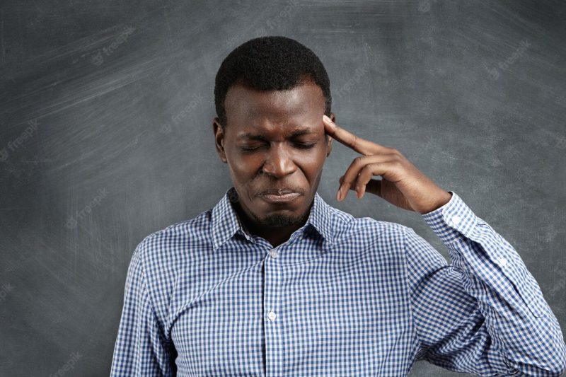 Stressed African businessman with painstaking expression struggling to remember something, closing his eyes tight and pressing finger on his temple as if having bad headache. Free Photo