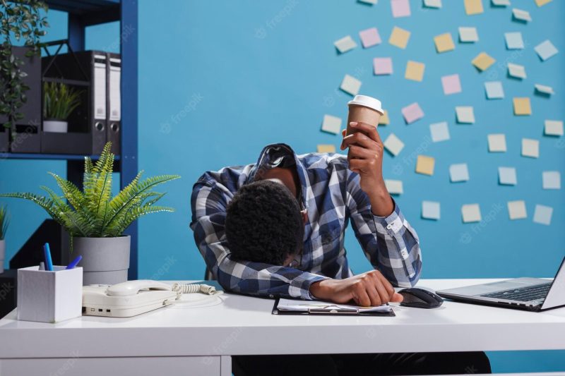 Stressed and fatigued team leader with burnout syndrome sitting in modern office workspace. tired and exhausted agency office employee falling asleep at desk because of overtime work Free Photo