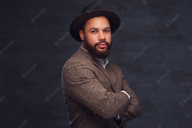 Studio portrait of handsome afro-american male in an elegant brown jacket and hat. isolated on a dark background. Free Photo