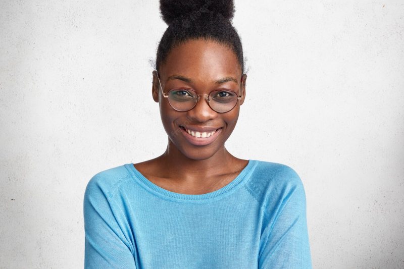 Studio shot of delighted satisfied dark skinned female worker, wears round big glasses, being glad to be promoted at work Free Photo