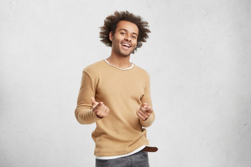 Stylish happy African American male wears casual clothes, points in camera with fore fingers Free Photo