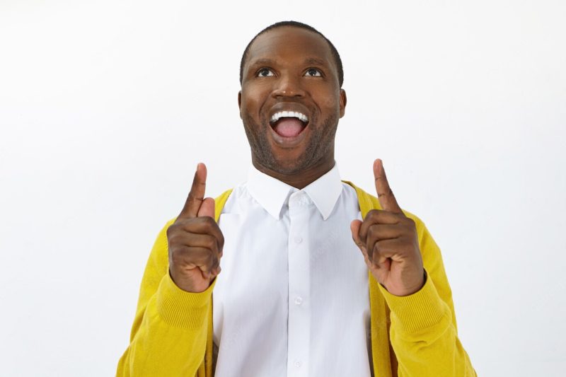 Success, joy and victory concept. studio shot of emotional funny african male looking up with mouth wide opened, expressing excitement and full disbelief, pointing both index fingers upwards Free Photo