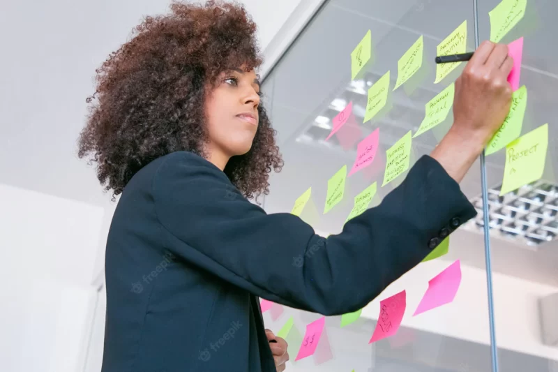 Successful pretty businesswoman writing on sticker with marker. thoughtful confident curly female manager sharing idea for project and making note. brainstorming, business and training concept Free Photo