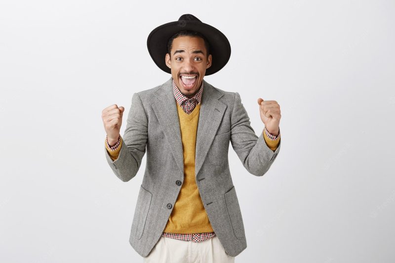 Successful winning African American man in suit celebrating victory, smiling thrilled and fist pump in rejoice Free Photo