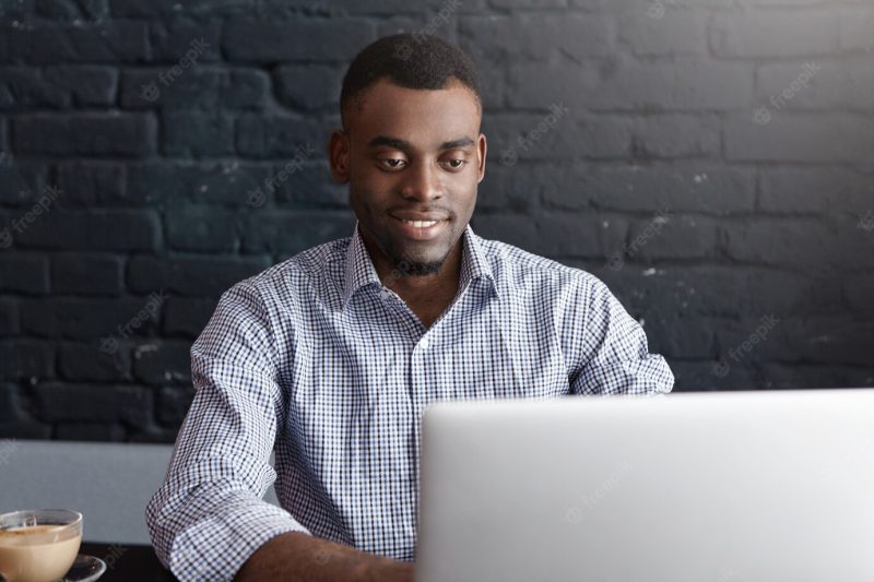 Successful young African entrepreneur sitting at cafe table, working on laptop Free Photo