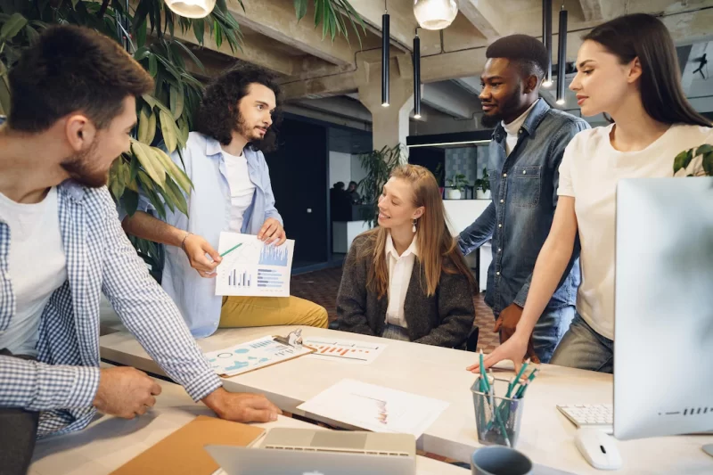 Team of diverse coworkers in modern office discuss their project together Free Photo